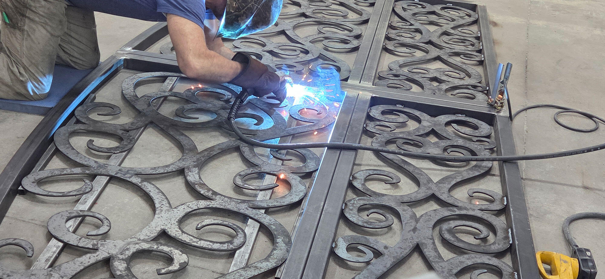 Jason Pedersen Welding Custom Ornamental Gate Panel | Titan Forge Utah Jason Pedersen welding a custom ornamental gate panel with decorative scrollwork, showcasing precision metal fabrication and craftsmanship at Titan Forge in Springville, Utah.